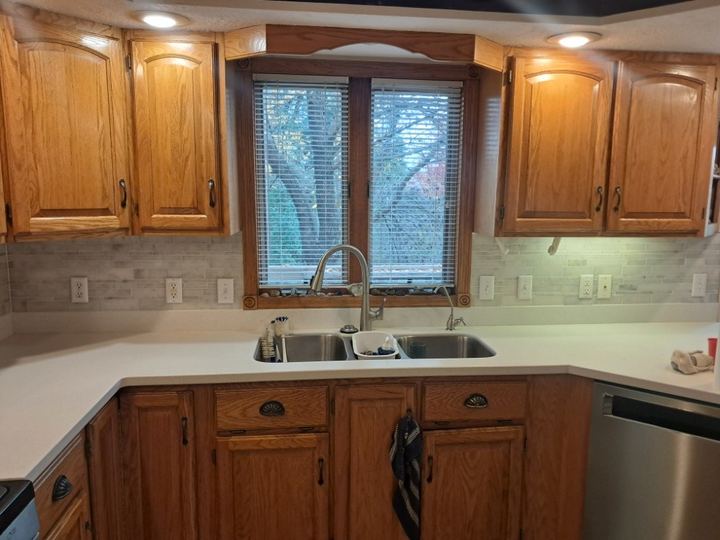 Kitchen with gray tile backsplash behind sink, white countertop, oak cabinets