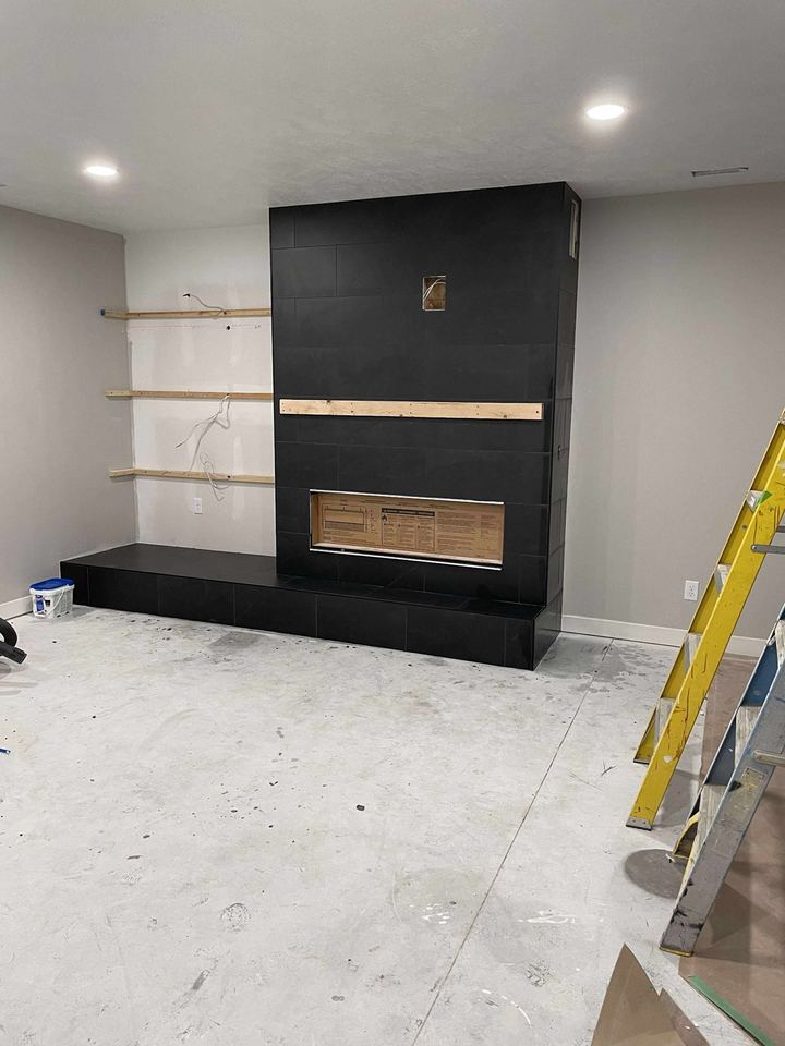 Black-tile fireplace surround on a wall with tile floor, work in progress